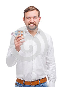 A guy with a smile in jeans holds a plate with pills on a white isolated background