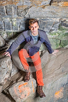 A young guy is standing in a cave of rocks, looking up and thinking