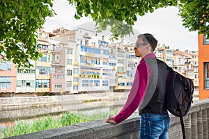 A young guy stands with a backpack on the river bank Onyar in Gi