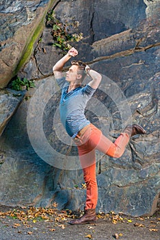 A young guy is stretching arms and legs, dancing like a robot in the front of rocky wall