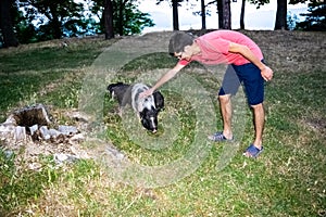 Young guy strokes a dwarf Vietnamese pot-bellied black and white mini pig, standing on green grass. Countryside and domestic