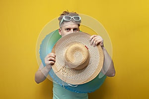 young guy in the summer on vacation with an inflatable swimming circle is shy and hides behind a big straw hat
