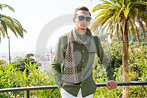A young guy with sunglasses and a scarf, a tourist, on a background of palm trees in Guell Park, architect Gaudi in Barcelona