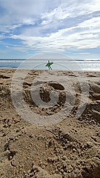 A young guy with a surfboard runs along the ocean in search of big waves