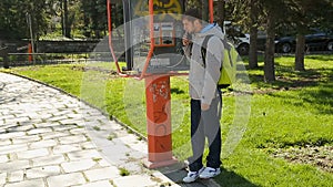 Young guy taking off receiver of payphone, standing and holding phone at ear