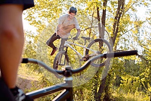 Young guy with tattoos, biker, jumps and performs tricks on a bike. view through bicycle frame. in the forest against the setting