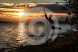 Young guy tourist jumps and enjoys a beautiful sunset over the lake. A midges fly around him, which glows in the rays