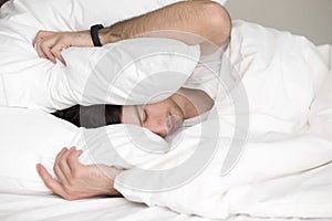 Young guy trying to sleep, covering his head with pillow