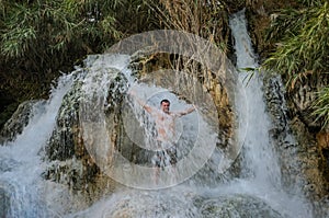 Young guy under the streams of a waterfall