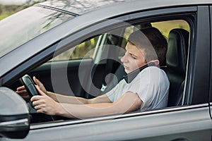 Young guy unsafe driving while talking on his phone in front of the steering wheel. Driver using his smartphone. Risk and danger