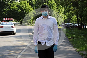 A young guy walks down the street on a summer day in a white shirt and a mask on his face. Mask mode.