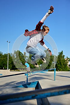 Young guy wearing rollerblades jumping from handrail on outdoor rollerdrome