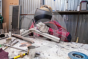 Young guy welder in a checkered red shirt welds a stainless steel pipe for car exhaust using agronomic welding to protect his eyes