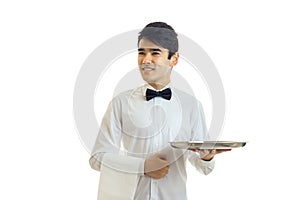 A young guy in a white shirt and black bow tie looks away smiling and holding a towel and tray