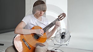 young guy in a white T-shirt learns to play guitar. online lessons on smartphone