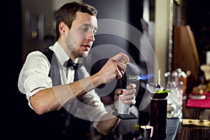 A young guy working as a bartender behind a bar is preparing drinks