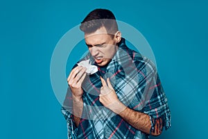 Young guy wrapped in plaid sneezes isolated