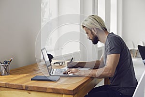 Young guy writing down main points from online business conference or educational webinar at desk indoors