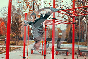 Young gymnast woman at playground hanging upside down on rings and doing splits in park at autumn