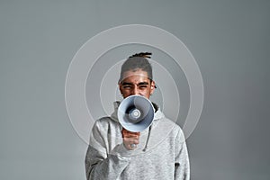 Young gypsy man with loudspeaker on light background