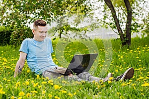 Young gyu freelincer at work on a laptop on a green grass and trees background