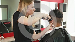 Young hair stylist shaves the back of the head of the client`s salon spa center