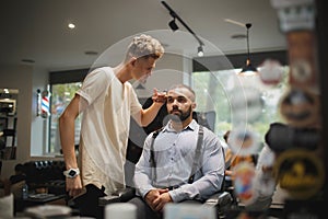 Young hairdresser cutting hair of a male client. A handsome hairstylist serving a client on a blurred barbershop