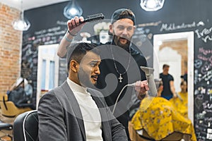 a young hairdresser holding a comb and a hair drier and making a new hairstyle for a client