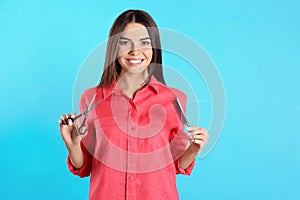 Young hairstylist holding professional scissors and comb on color background