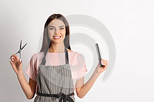 Young hairstylist holding professional scissors and comb on light