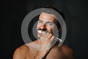 Young half-naked man smiling while brushing his teeth