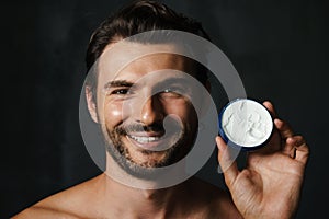 Young half-naked man smiling while showing face cream