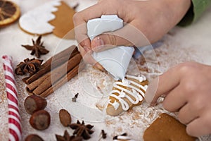 Young hands decorate gingerbread cookie with white icing