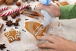Young hands decorate gingerbread cookies with white icing applied from plastic bag