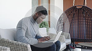 Young handsom black man working on the laptop on his balcony while drinking coffee