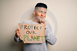 Young handsome activist latin man holding banner asking to protect our planet serious face thinking about question, very confused