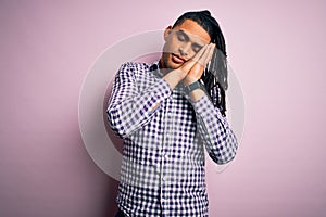 Young handsome african american afro man with dreadlocks wearing casual shirt sleeping tired dreaming and posing with hands