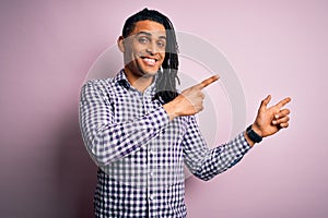 Young handsome african american afro man with dreadlocks wearing casual shirt smiling and looking at the camera pointing with two