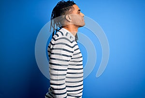 Young handsome african american afro man with dreadlocks wearing casual striped sweater looking to side, relax profile pose with