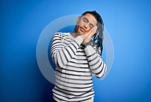 Young handsome african american afro man with dreadlocks wearing casual striped sweater sleeping tired dreaming and posing with