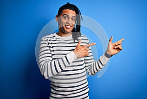 Young handsome african american afro man with dreadlocks wearing casual striped sweater smiling and looking at the camera pointing
