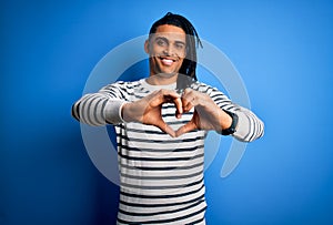 Young handsome african american afro man with dreadlocks wearing casual striped sweater smiling in love doing heart symbol shape