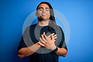 Young handsome african american afro man with dreadlocks wearing casual t-shirt smiling with hands on chest with closed eyes and