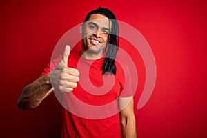 Young handsome african american afro man with dreadlocks wearing red casual t-shirt doing happy thumbs up gesture with hand
