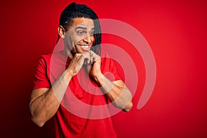Young handsome african american afro man with dreadlocks wearing red casual t-shirt laughing nervous and excited with hands on