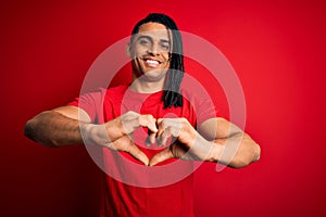 Young handsome african american afro man with dreadlocks wearing red casual t-shirt smiling in love doing heart symbol shape with
