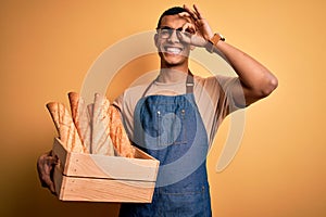 Young handsome african american bakery man holding wooden box with healthy fresh bread with happy face smiling doing ok sign with