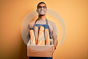Young handsome african american bakery man holding wooden box with healthy fresh bread with a happy face standing and smiling with