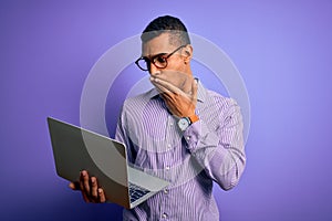 Young handsome african american business man working using laptop over purple background cover mouth with hand shocked with shame