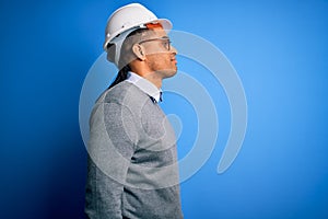 Young handsome african american engineer man with dreadlocks wearing safety helmet looking to side, relax profile pose with